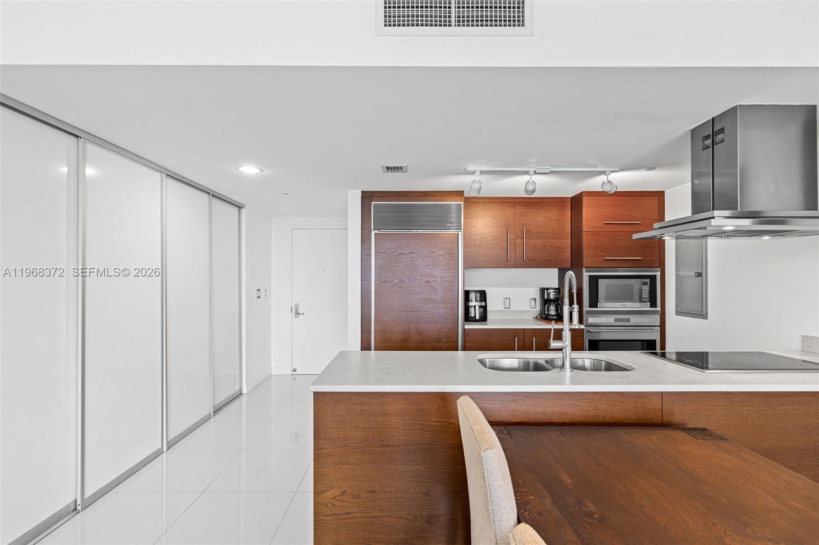 A modern kitchen features wood cabinetry, stainless steel appliances, and a white stone island — 495 Brickell Ave # 905, Miami FL 33131, MIAMI, FL