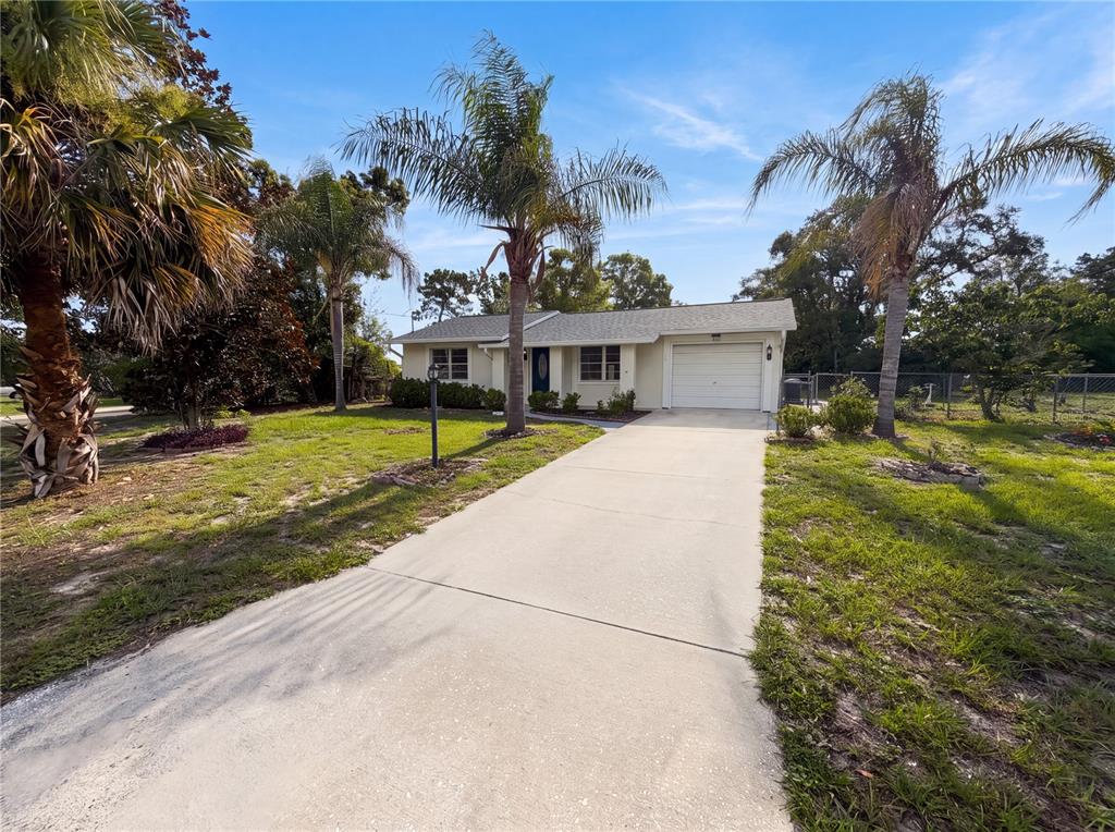 A single-story house with a white exterior, a concrete driveway, and several palm trees — 5304 HARBINGER ROAD, SPRING HILL, FL