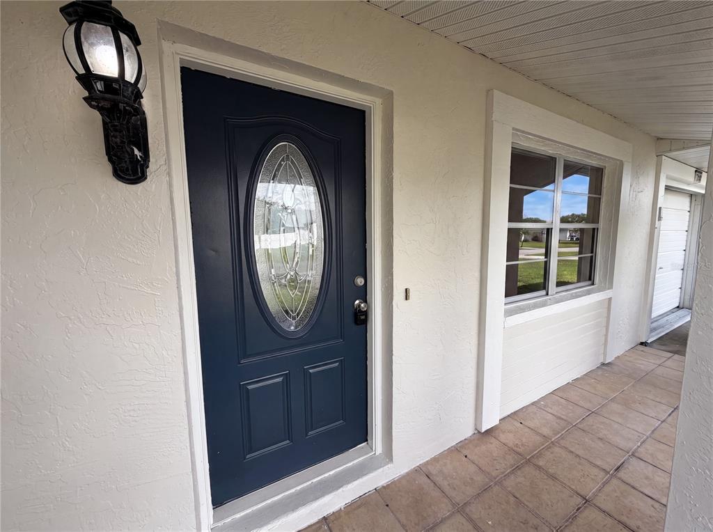 A dark blue front door with an oval glass insert sits on a tiled porch — 5304 HARBINGER ROAD, SPRING HILL, FL