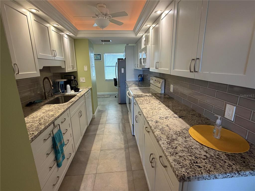 A galley kitchen features white cabinets, granite countertops, a gray tile backsplash, and tile flooring — 204 3RD STREET W UNIT 405, BRADENTON, FL