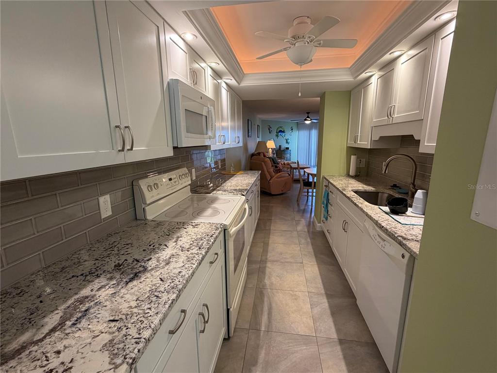 A galley kitchen features white cabinets, granite countertops, a subway tile backsplash, and stainless appliances — 204 3RD STREET W UNIT 405, BRADENTON, FL