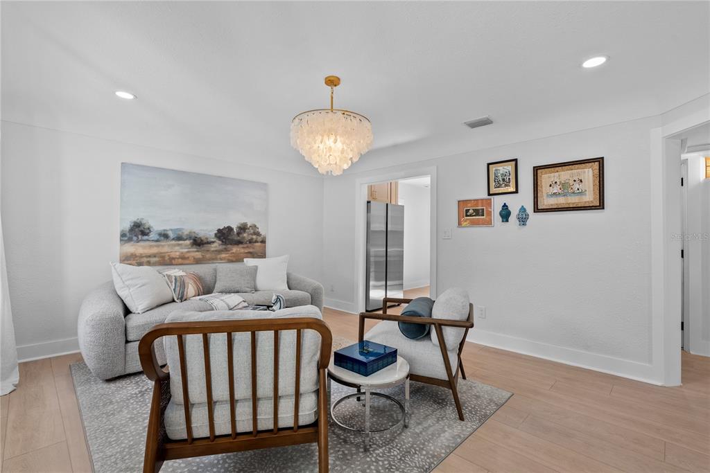 A living room features light wood floors, a textured chandelier, and a curved gray sofa — 1211 16TH AVENUE N, ST PETERSBURG, FL