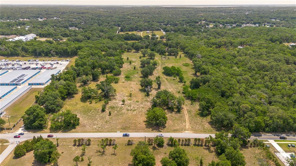An aerial view shows a large, partially wooded vacant lot bordered by a road — 0 ROLLING ACRES ROAD, LADY LAKE, FL