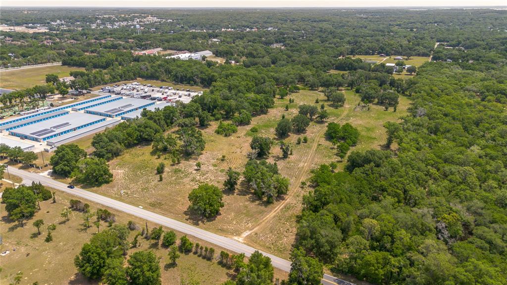 An aerial view shows a vacant, grassy lot bordered by a road, trees, and buildings — 0 ROLLING ACRES ROAD, LADY LAKE, FL