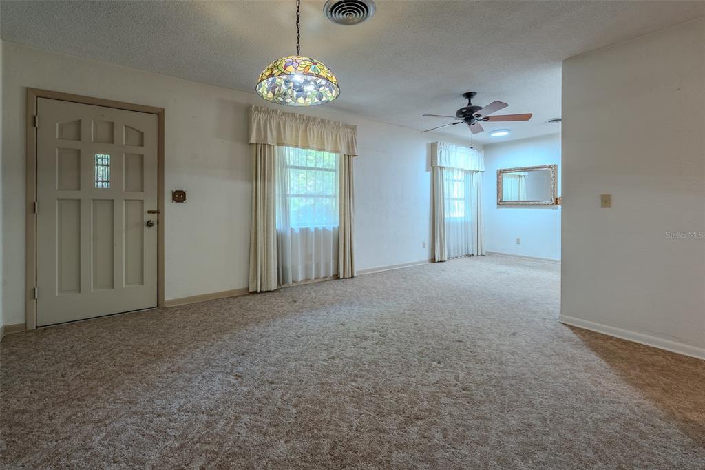 A carpeted living room features a stained-glass pendant light, two windows with curtains, and a door — 2217 NW 52 STREET, OCALA, FL