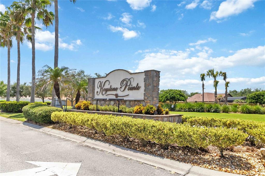 A stone monument sign for Keystone Pointe stands near a road with palm trees — 3014 SAND STONE CIRCLE, ST CLOUD, FL