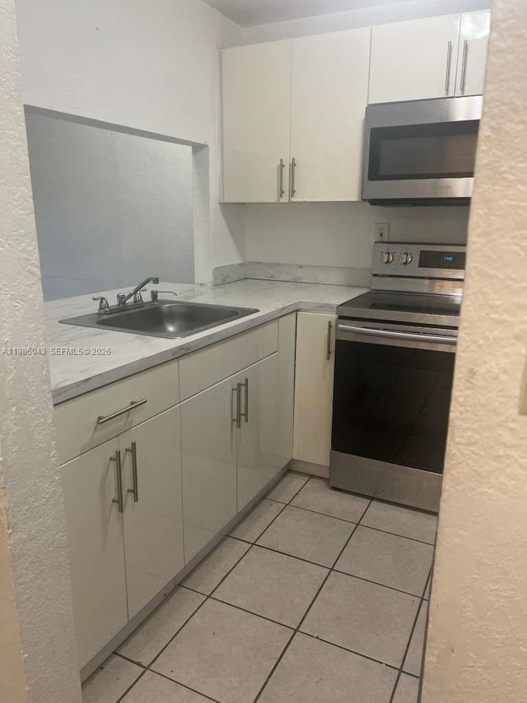 A small kitchen features white cabinets, stainless steel appliances, and a marble-patterned countertop — 4550 NW 9th St # 114E, Miami FL 33126, MIAMI, FL