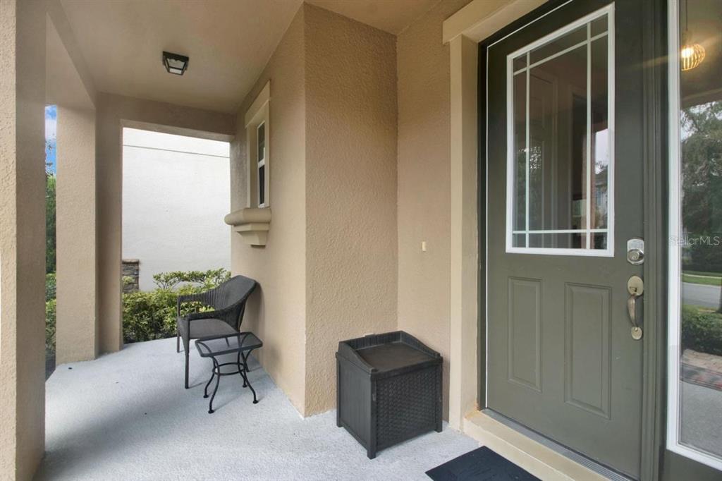 A covered front porch features a dark green door, a small chair, and a storage bin — 9021 FLAMINGO KEY WAY, KISSIMMEE, FL