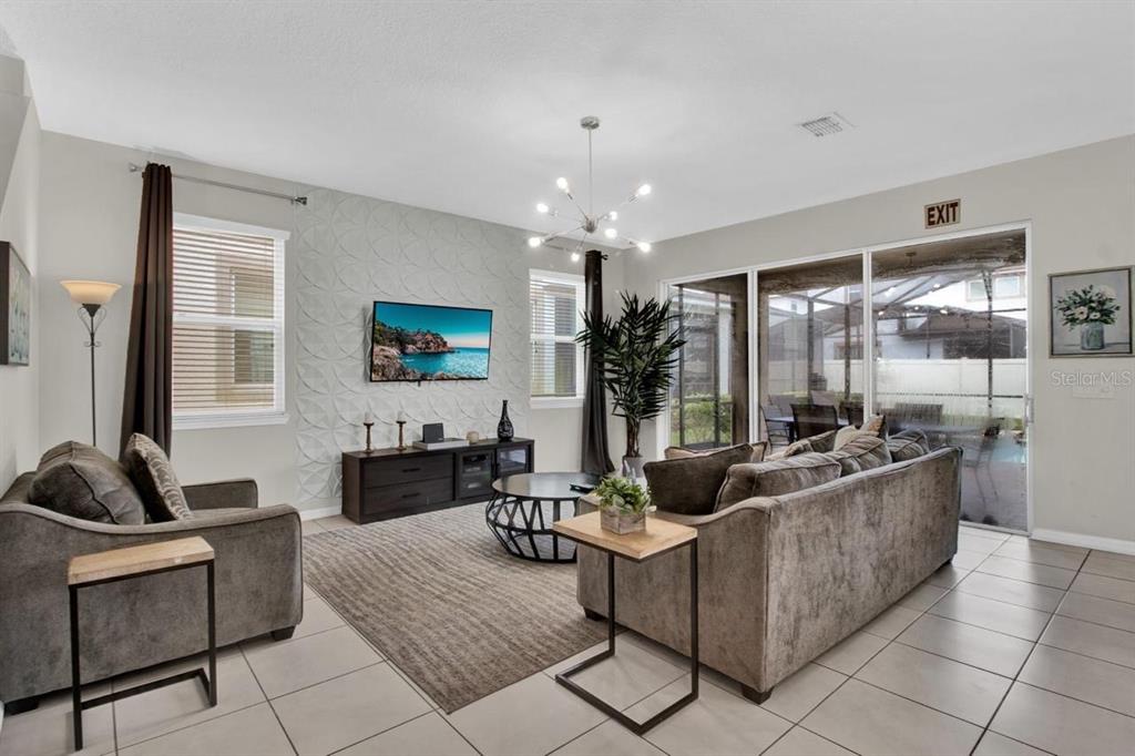 A living room features a textured accent wall, a television, and sliding glass doors — 9021 FLAMINGO KEY WAY, KISSIMMEE, FL