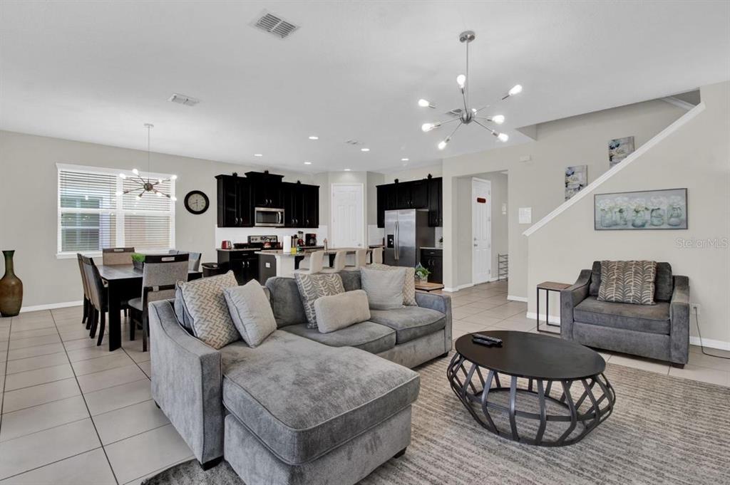 An open-concept living room and kitchen featuring grey furniture, tile flooring, and dark cabinetry — 9021 FLAMINGO KEY WAY, KISSIMMEE, FL