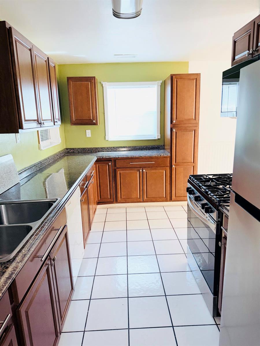 A kitchen features wood cabinets, dark countertops, white tile flooring, and a green accent wall — 5755 Winfield Boulevard, Margate FL 33063, MARGATE, FL