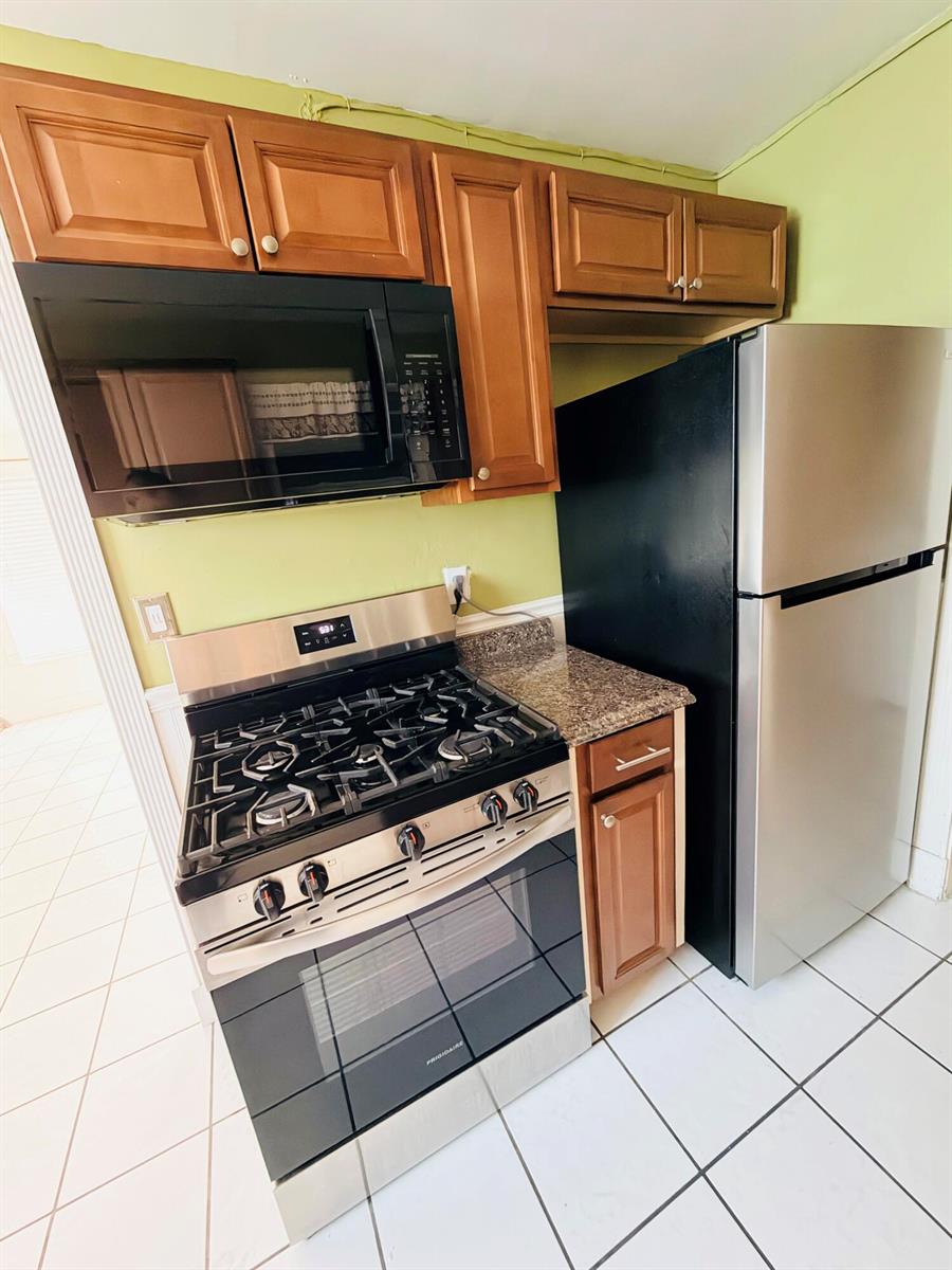 A kitchen features wood cabinets, stainless steel appliances, granite countertops, and light green walls — 5755 Winfield Boulevard, Margate FL 33063, MARGATE, FL