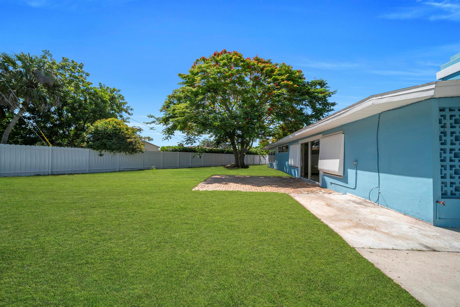 A blue house exterior features a brick patio, a large tree, and a white fence — 139 E Lake Drive, Lehigh Acres FL 33936, LEHIGH ACRES, FL