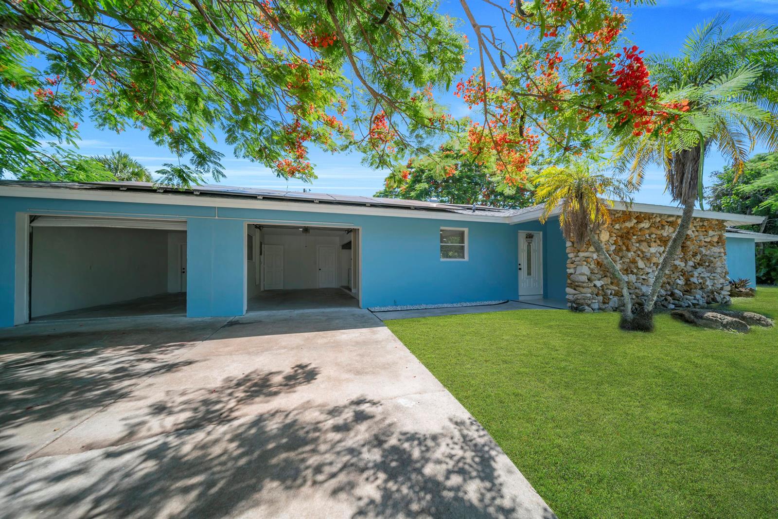 A blue single-story house features a two-car garage, a stone facade, and a front lawn — 139 E Lake Drive, Lehigh Acres FL 33936, LEHIGH ACRES, FL