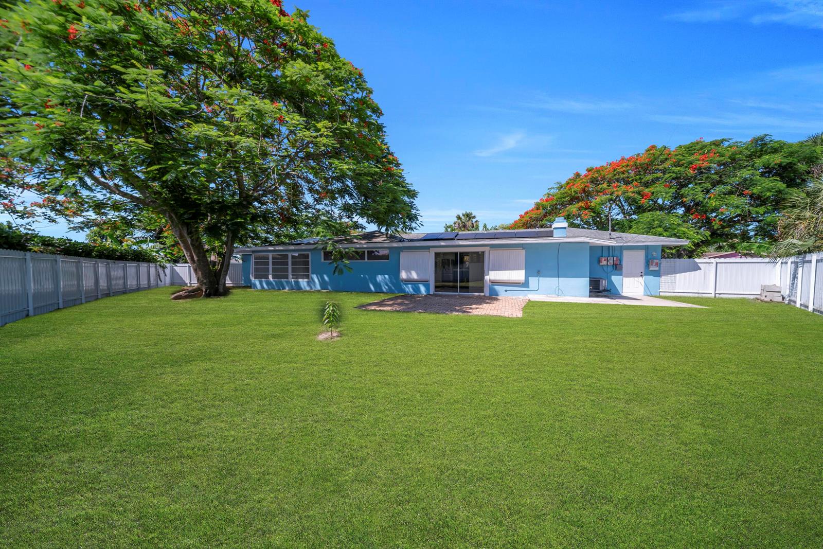 A blue single-story house with a large backyard, a brick patio, and two flowering trees — 139 E Lake Drive, Lehigh Acres FL 33936, LEHIGH ACRES, FL