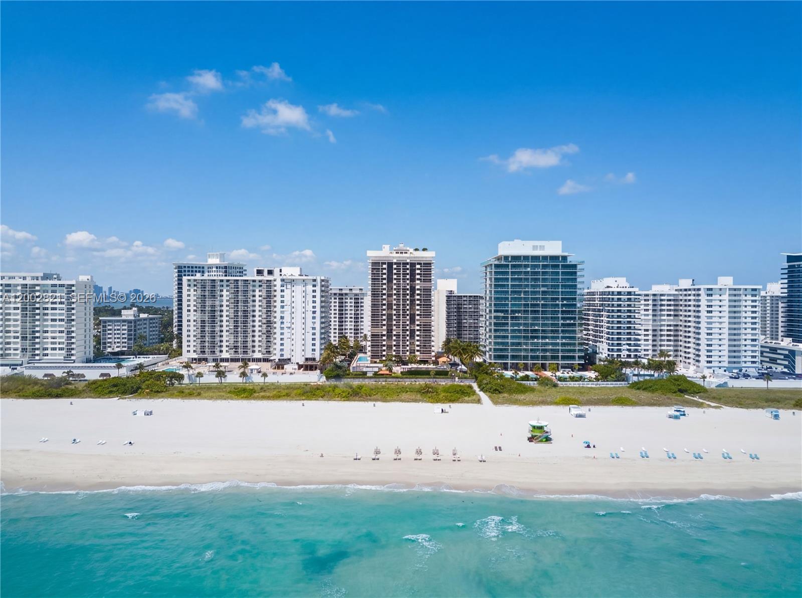 An aerial view shows a sandy beach with a lifeguard tower in front of several high-rise buildings — 5757 Collins Ave # 1104, Miami Beach FL 33140, MIAMI BEACH, FL