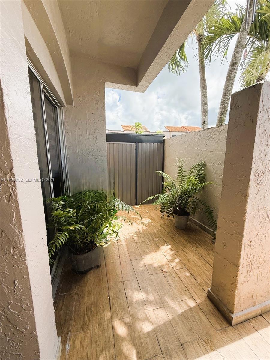 A covered patio features wood-look tile flooring, two potted ferns, and a metal privacy gate — 6217 SW 128th Pl, Miami FL 33183, MIAMI, FL