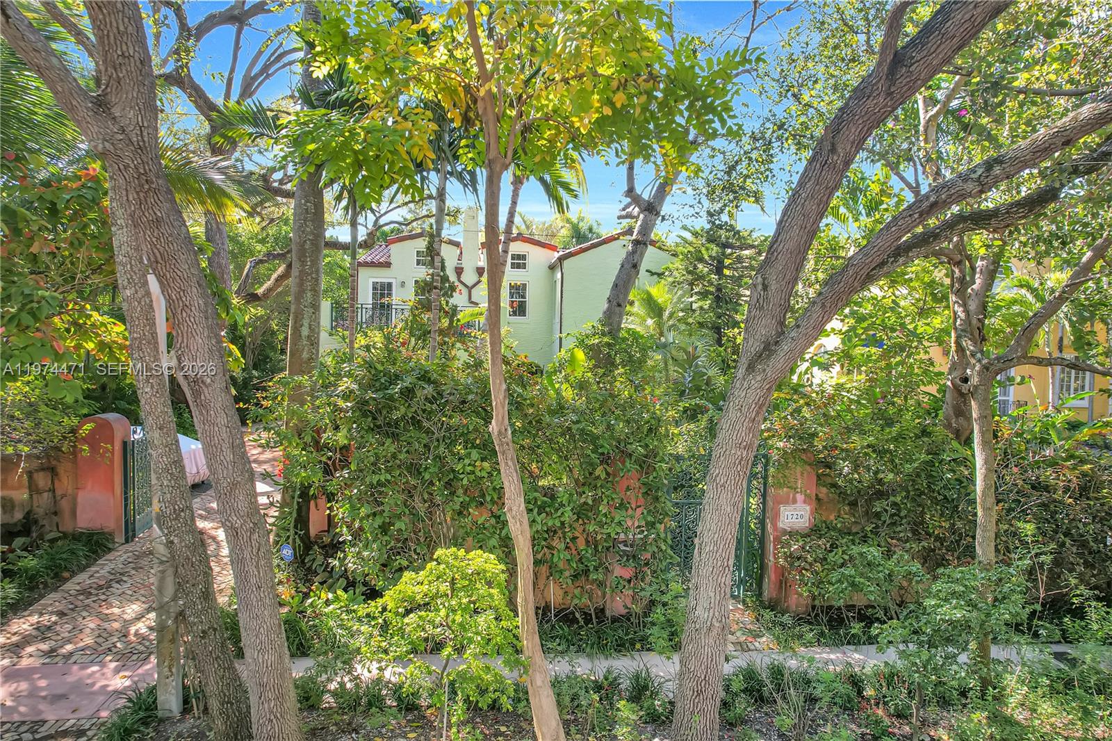 A stone patio with outdoor furniture sits beside a two-story house with lush landscaping — 1720 Espanola Dr, Miami FL 33133, MIAMI, FL