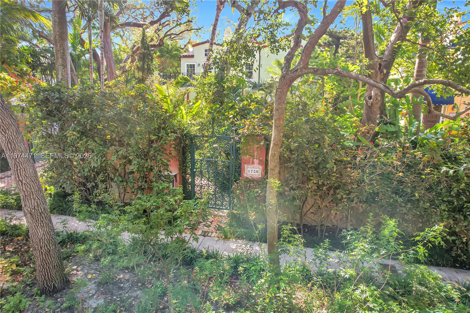 A brick walkway leads through lush landscaping toward a house entrance behind a gate — 1720 Espanola Dr, Miami FL 33133, MIAMI, FL