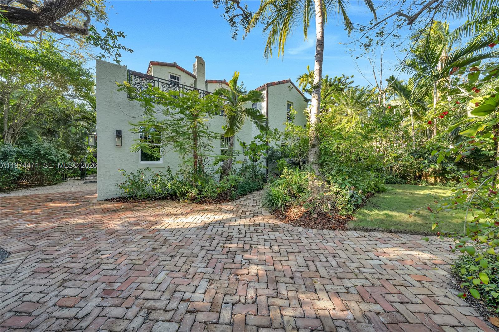 A two-story stucco house features a brick driveway and lush landscaping under a blue sky — 1720 Espanola Dr, Miami FL 33133, MIAMI, FL