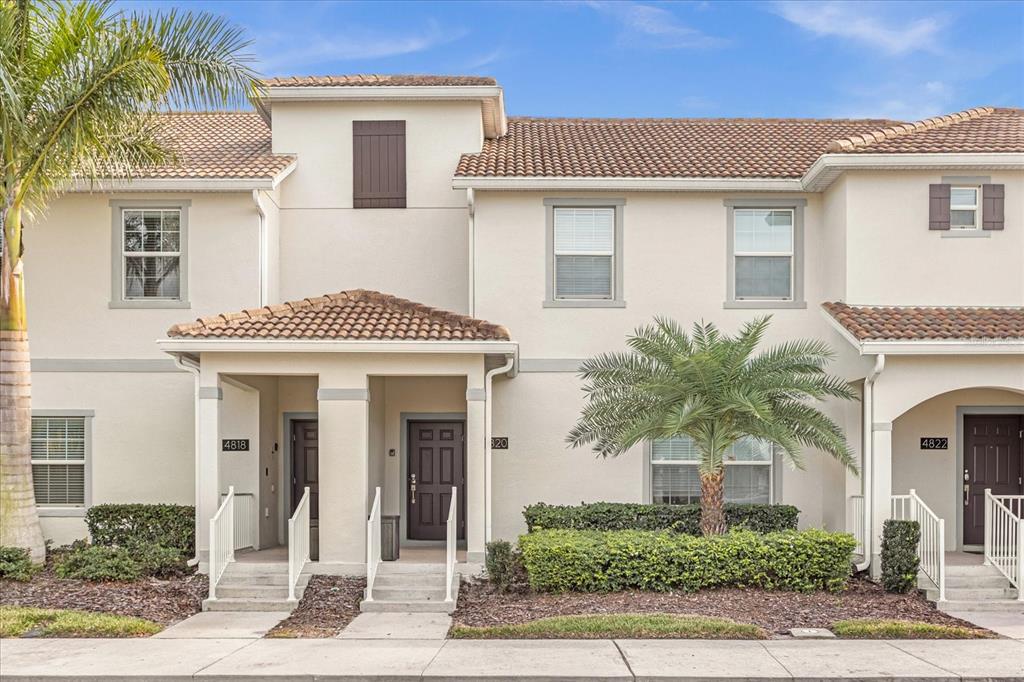 A two-story townhouse exterior with a tiled roof, beige stucco walls, and palm trees — 4820 LOVE STOREY LANE, KISSIMMEE, FL