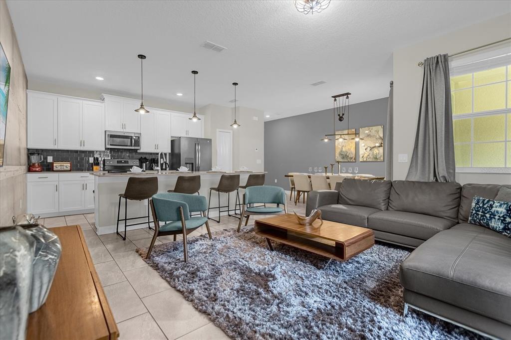 An open-concept living room and kitchen featuring a gray sectional, dining area, and breakfast bar — 4820 LOVE STOREY LANE, KISSIMMEE, FL