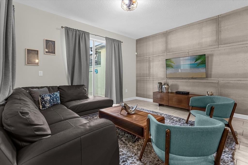 A living room features a dark leather sectional, two teal chairs, and a concrete-paneled wall — 4820 LOVE STOREY LANE, KISSIMMEE, FL