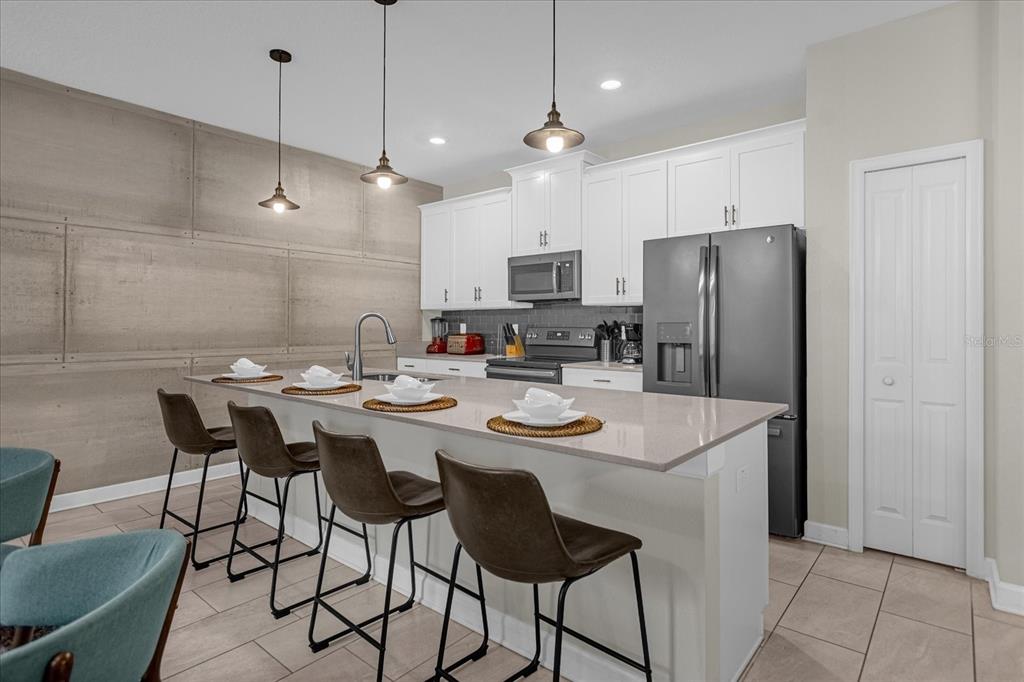 A kitchen features white cabinets, a quartz island with four stools, and a concrete-textured wall — 4820 LOVE STOREY LANE, KISSIMMEE, FL
