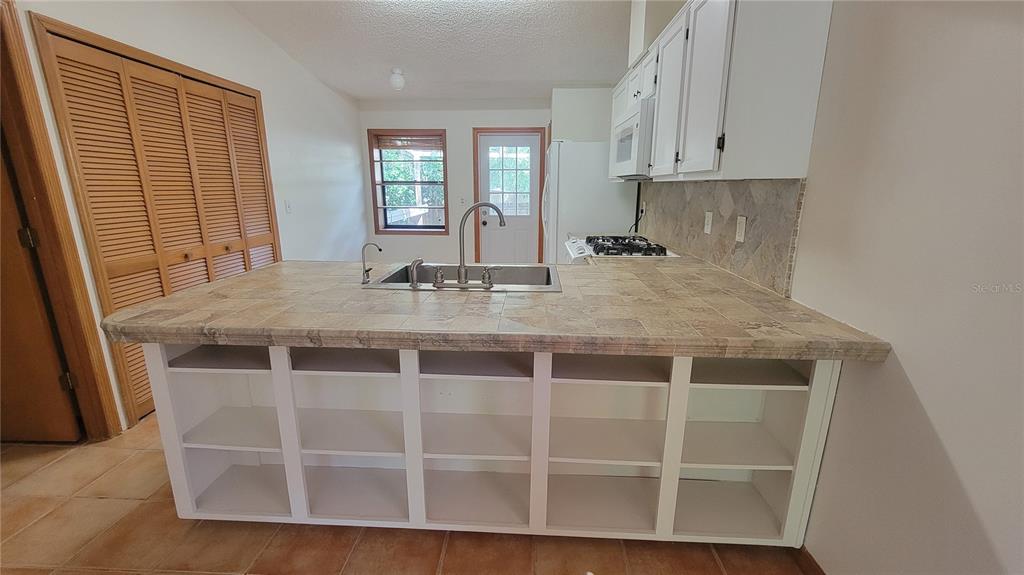 A kitchen features a tiled island with an integrated sink and open white shelving — 1011 LOVE LANE UNIT 31, APOPKA, FL