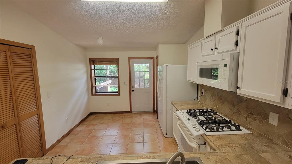 A kitchen with white cabinets, a gas stove, tile countertops, and an adjacent dining area — 1011 LOVE LANE UNIT 31, APOPKA, FL