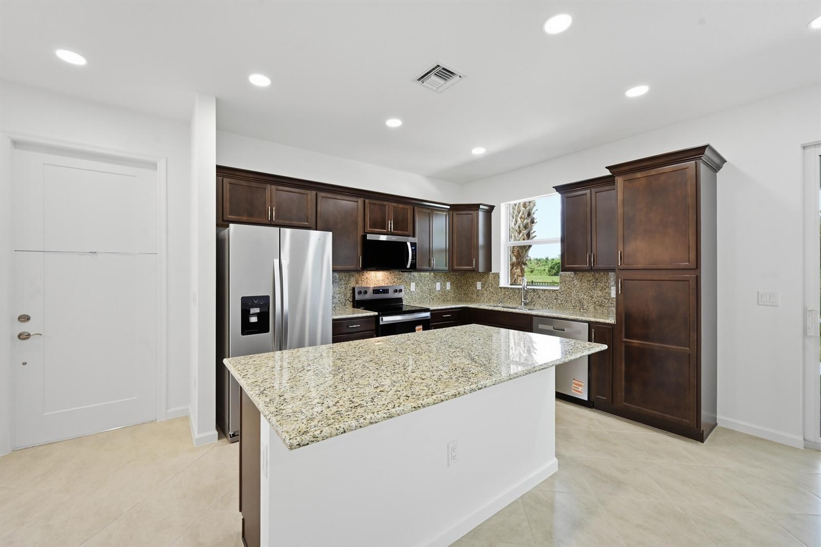 A kitchen features dark wood cabinets, granite countertops, a central island, and stainless steel appliances — 4356 Brookgreen Square, Westlake FL 33470, WESTLAKE, FL