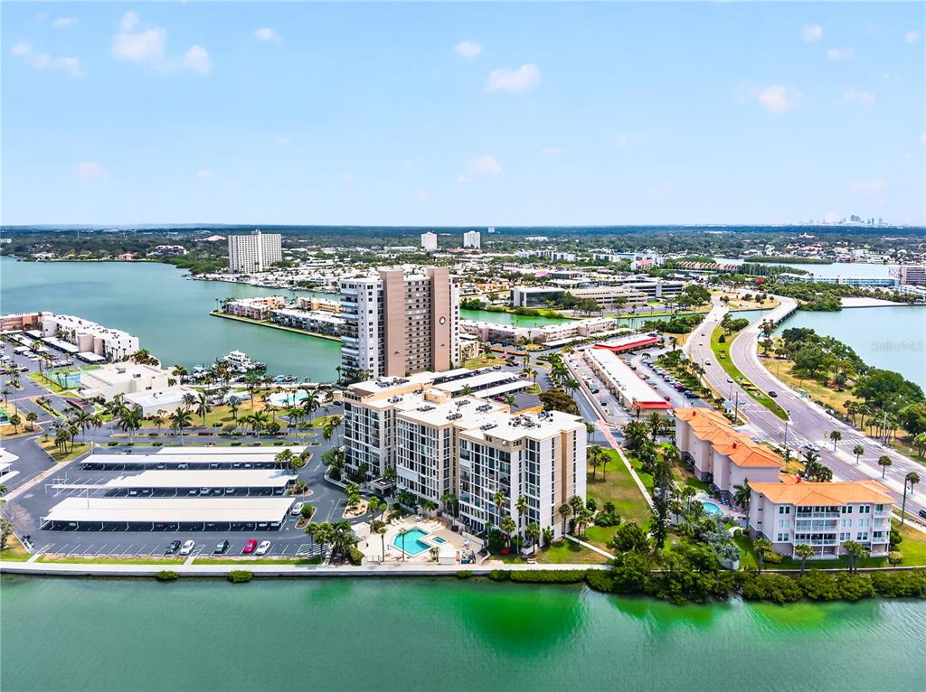 An aerial view shows waterfront apartment buildings, a swimming pool, parking lots, and a road — 7400 SUN ISLAND DRIVE S UNIT 203, SOUTH PASADENA, FL
