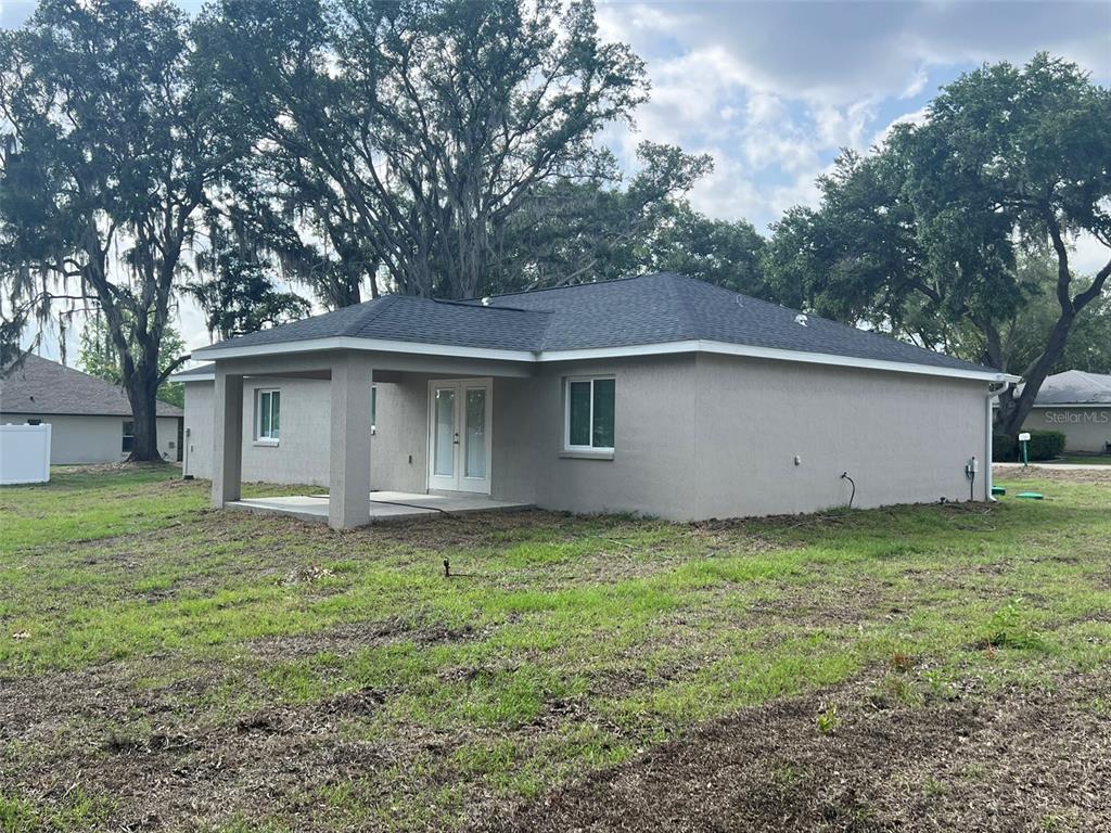 The back exterior of a single-story house features a covered patio and a grassy yard — 8640 SE 157 PLACE, SUMMERFIELD, FL