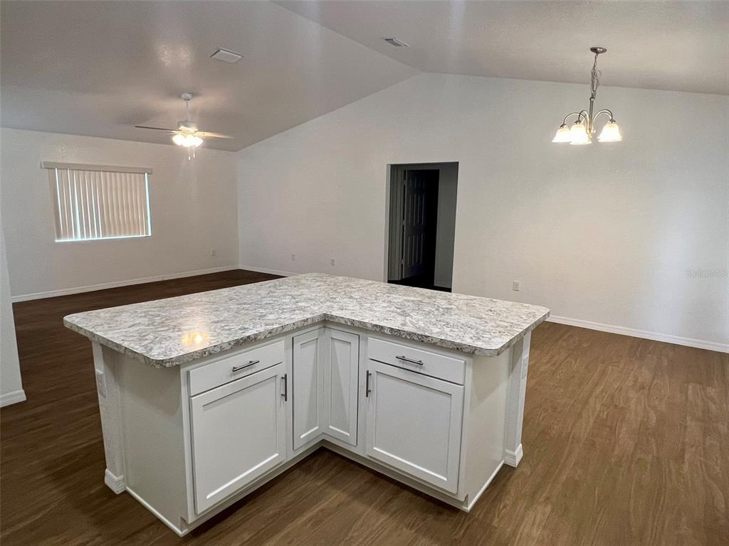 A kitchen island with white cabinets and a stone countertop sits in an open room — 8640 SE 157 PLACE, SUMMERFIELD, FL