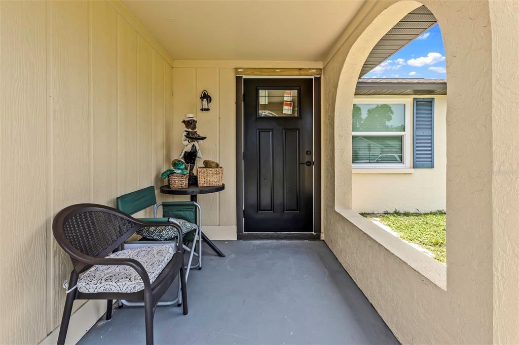 A covered front porch features a black door, two chairs, and a small side table — 1032 ELAINE STREET, VENICE, FL