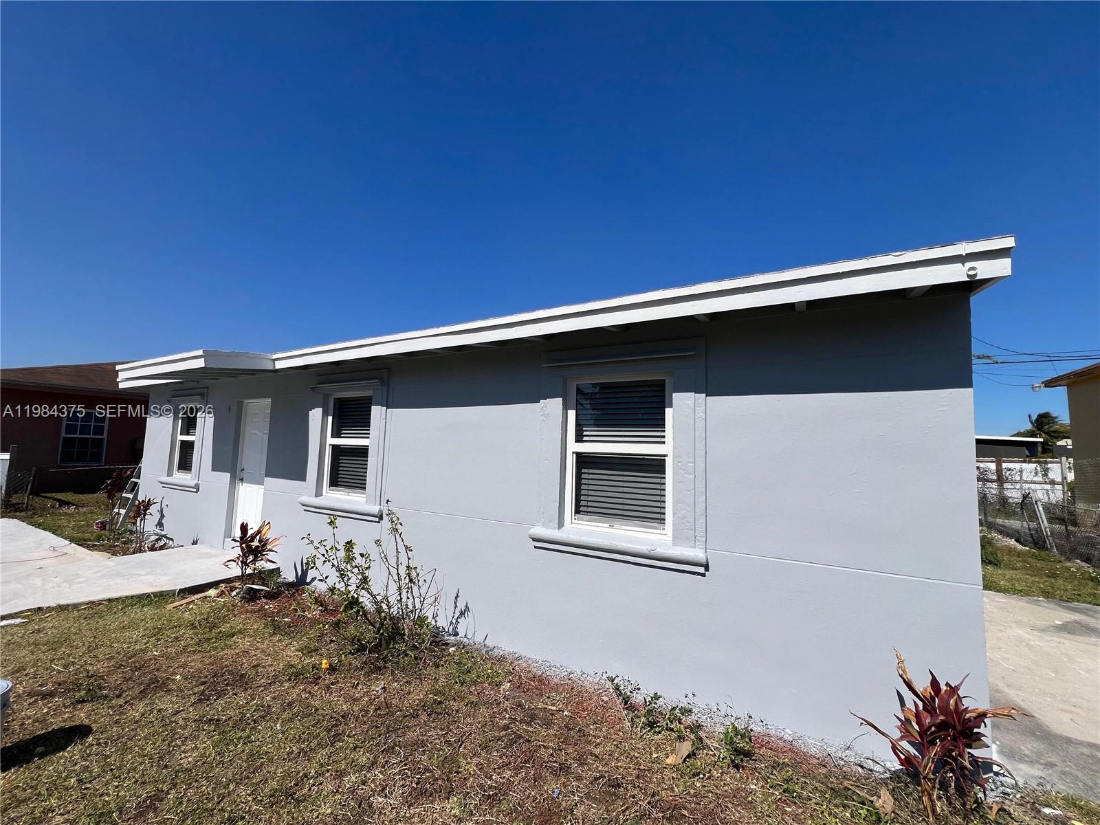 A gray, single-story house exterior features white trim, a white door, and two windows — 361 NW 16th St, Pompano Beach FL 33060, POMPANO BEACH, FL