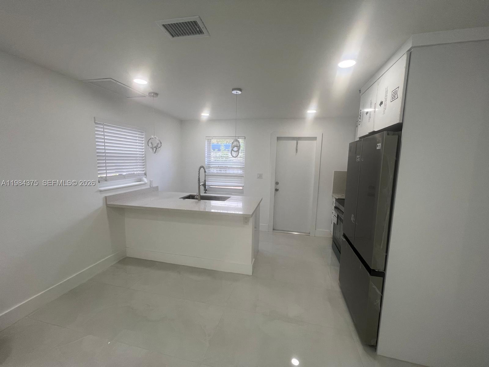 A modern kitchen features white cabinets, a quartz island, stainless steel appliances, and tile flooring — 361 NW 16th St, Pompano Beach FL 33060, POMPANO BEACH, FL
