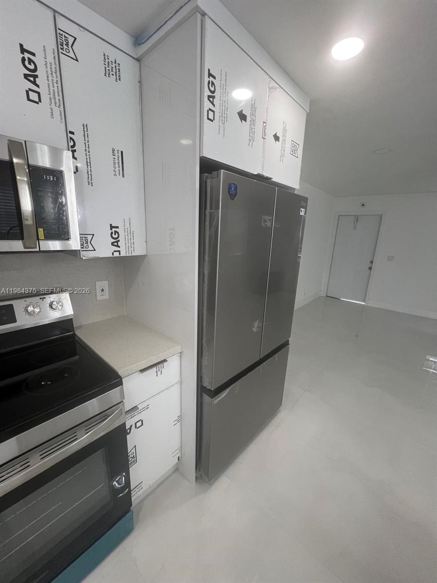 A kitchen features stainless steel appliances, white cabinetry with protective film, and light-colored tile flooring — 361 NW 16th St, Pompano Beach FL 33060, POMPANO BEACH, FL