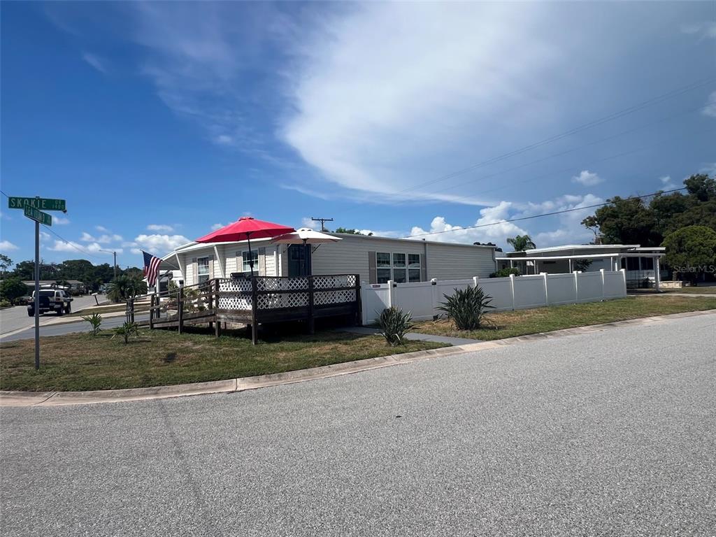 A single-story manufactured home features a wooden deck with umbrellas and a white vinyl fence — 4906 SEA ISLAND AVENUE, SARASOTA, FL