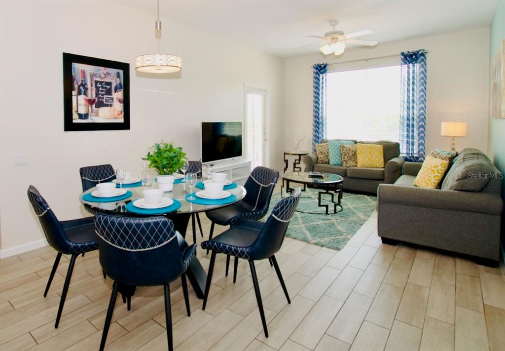 An open-concept living and dining area features a glass table, blue chairs, and gray sofas — 4802 CAYVIEW AVENUE UNIT 204, ORLANDO, FL