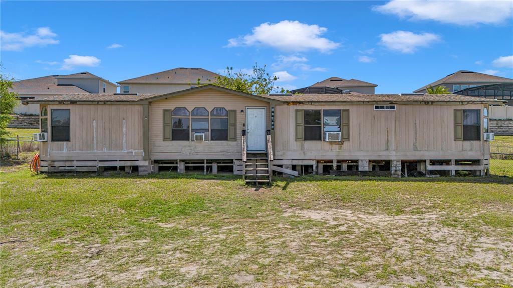 A single-story manufactured home with tan siding sits on a raised foundation in a yard — 12606 S GRASSY LAKE ROAD, MINNEOLA, FL
