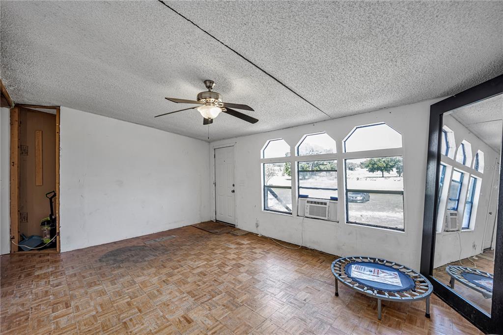 A room with parquet flooring, a ceiling fan, and a large mirror reflecting a window — 12606 S GRASSY LAKE ROAD, MINNEOLA, FL
