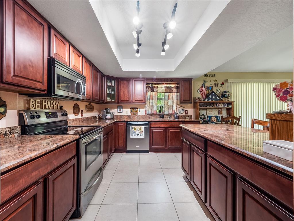 A kitchen features dark wood cabinets, granite countertops, stainless steel appliances, and tile flooring — 5845 LAKE LIZZIE DRIVE, ST CLOUD, FL