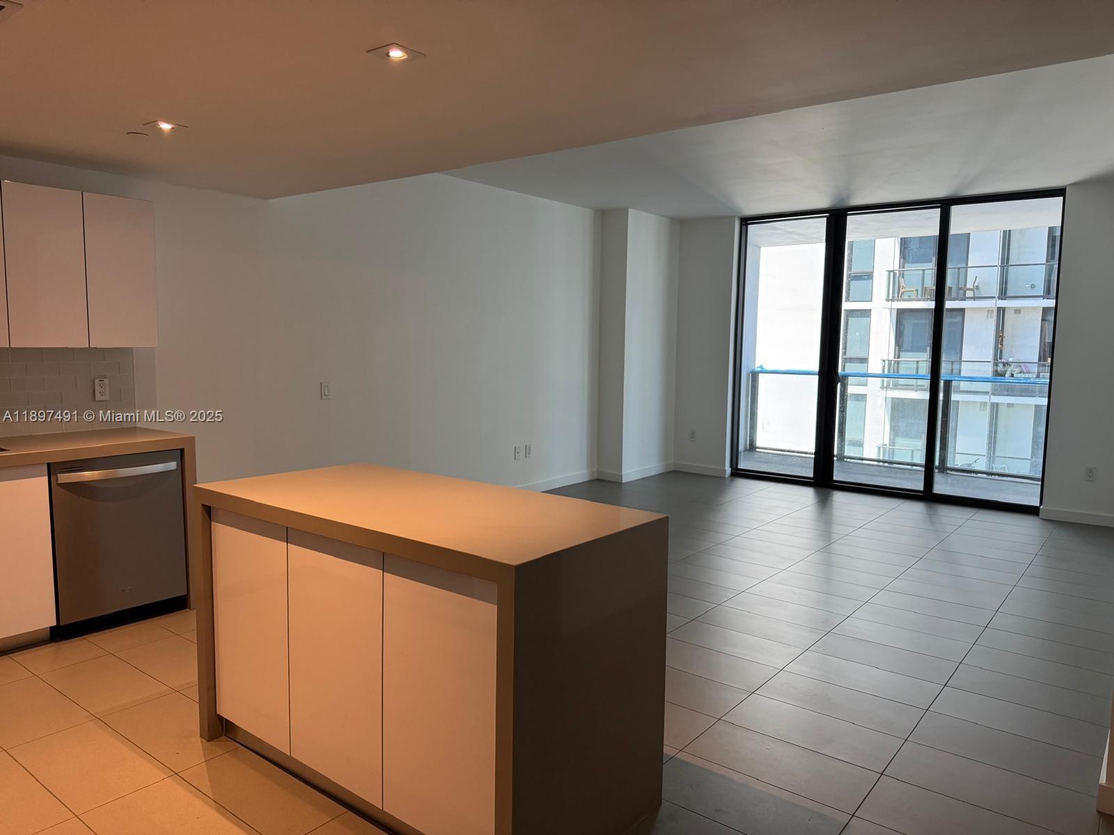 A modern kitchen island and cabinetry face an open living area with large glass doors — 1600 NE 1st Ave # 2217, Miami FL 33132, MIAMI, FL