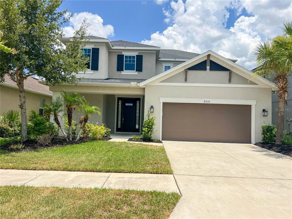 A two-story suburban house features a tan stucco exterior, a two-car garage, and dark shutters — 8033 CLEMENTINE LANE, TAMPA, FL