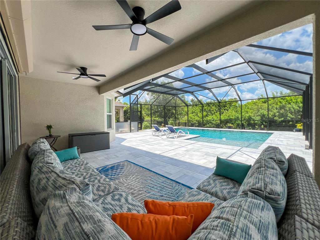A covered patio with outdoor seating overlooks a screened-in swimming pool and backyard — 8033 CLEMENTINE LANE, TAMPA, FL