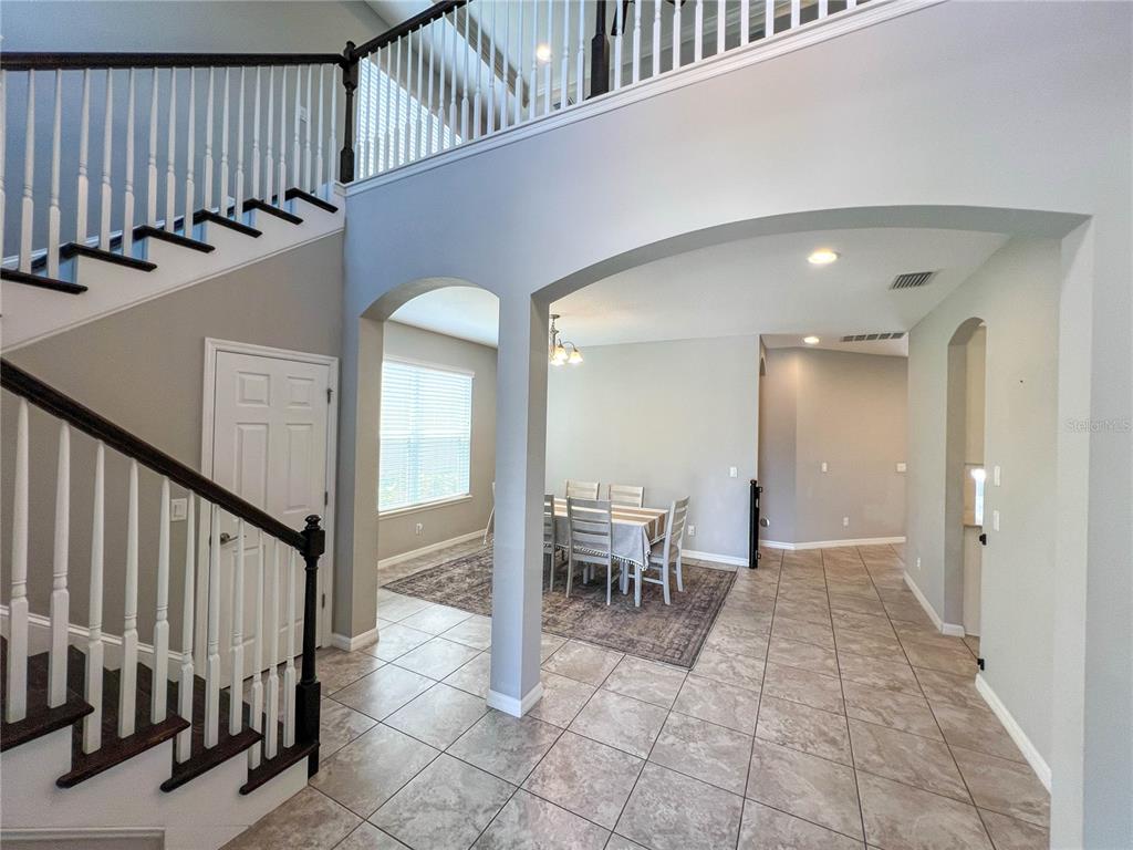 A foyer with a staircase leads to a dining area featuring tiled floors and arches — 8033 CLEMENTINE LANE, TAMPA, FL