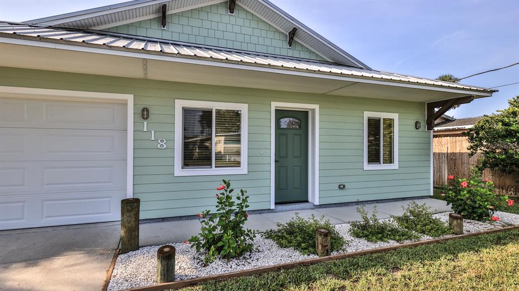 A light green house exterior features a white garage door, a dark green door, and landscaping — 118 SNYDER STREET, EDGEWATER, FL