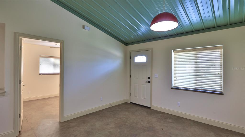 A room with a sloped metal ceiling, concrete floors, a white door, and a window — 118 SNYDER STREET, EDGEWATER, FL