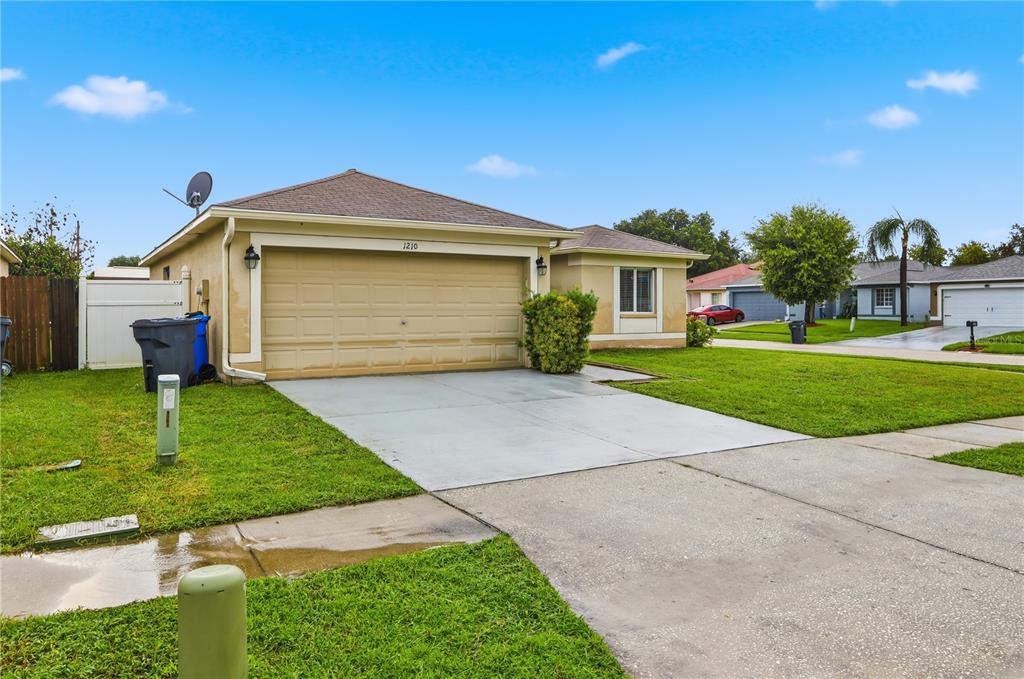 A single-story house with a beige exterior, a two-car garage, and a concrete driveway — 1210 BLUFIELD AVENUE, BRANDON, FL